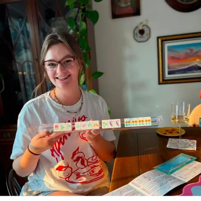 Cassidy at her table holding a rack of colorful mahjong tiles